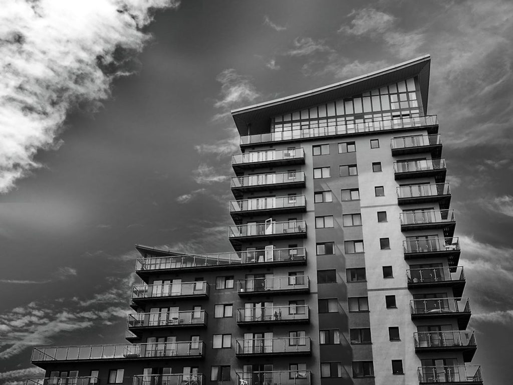 Monochrome photo of a modern high-rise apartment building with dynamic sky.